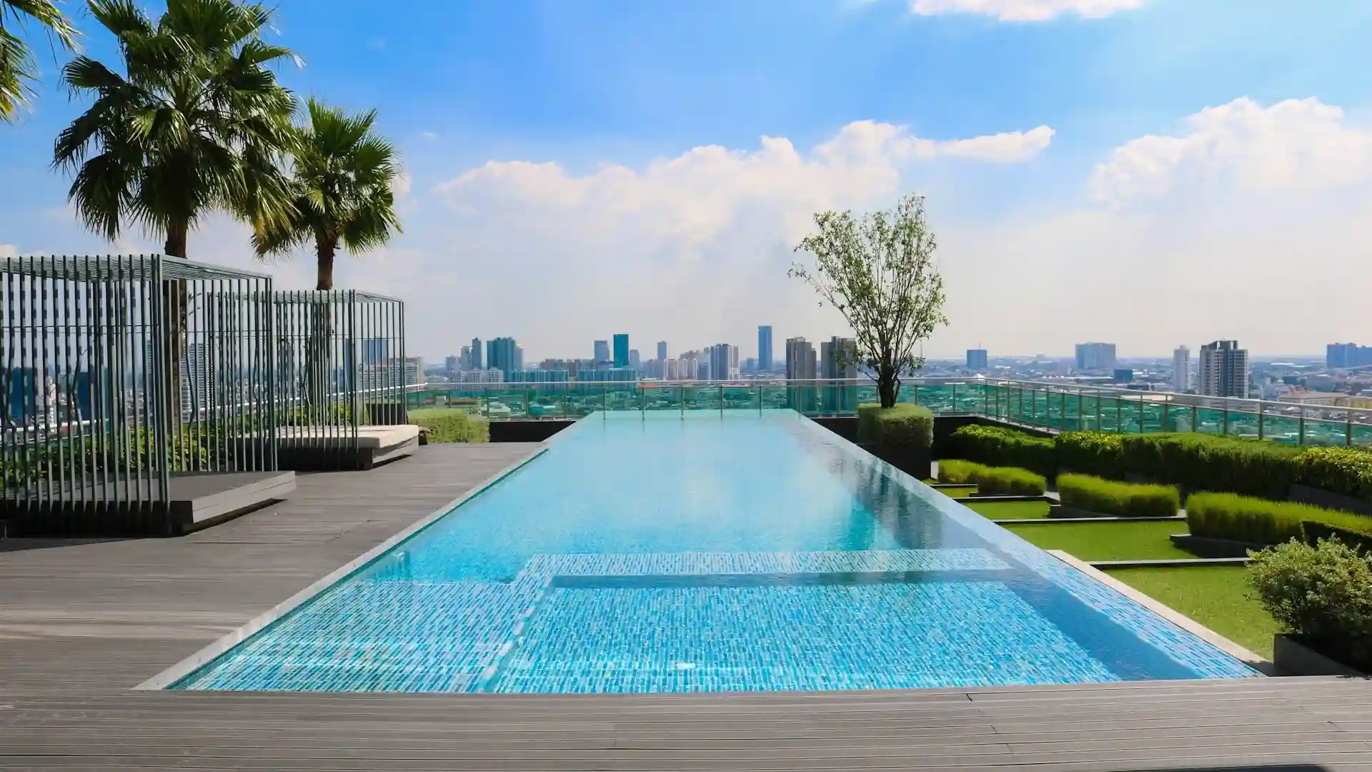 Rooftop infinity swimming pool at L&T Island Cove with panoramic city views, flanked by palm trees and modern lounge areas, epitomizing upscale urban living.